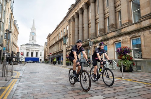 Jim and Murray cycling through Glasgow city centre at the start of their ride